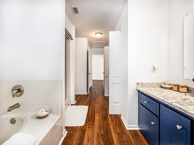 bathroom with vanity, wood-type flooring, and a relaxing tiled tub