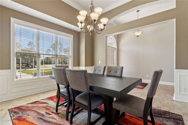 dining room featuring a notable chandelier, crown molding, wainscoting, a decorative wall, and arched walkways