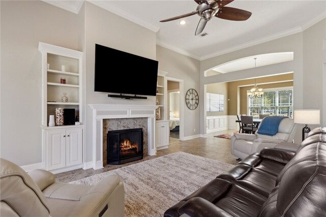 living area featuring crown molding, a fireplace, built in features, ceiling fan with notable chandelier, and visible vents