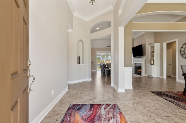 entrance foyer featuring a high ceiling, a warm lit fireplace, crown molding, and baseboards
