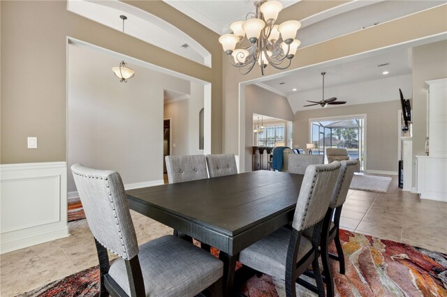 dining room with light tile patterned floors, ornamental molding, ceiling fan with notable chandelier, a wainscoted wall, and a decorative wall