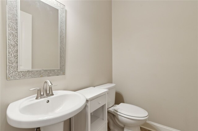bathroom with baseboards, toilet, and a sink
