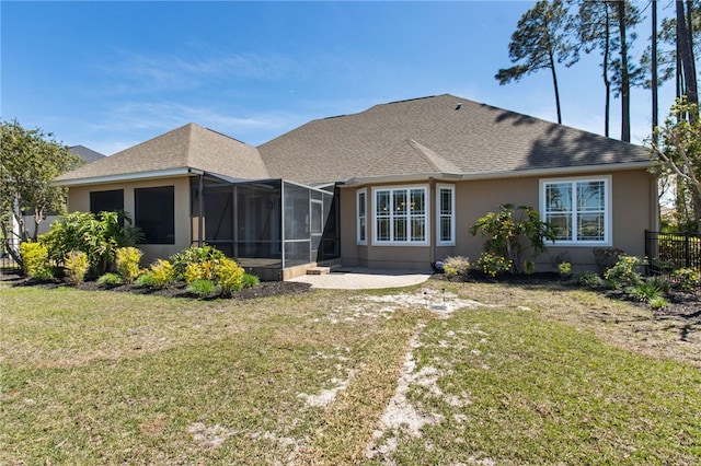 rear view of house with stucco siding, a shingled roof, a sunroom, a patio, and a lawn