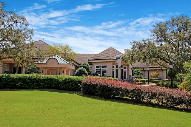 back of house with stucco siding, a tiled roof, and a yard
