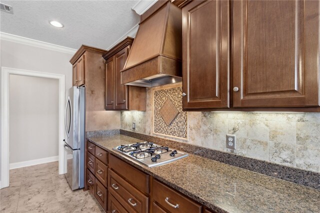 kitchen with decorative backsplash, custom exhaust hood, ornamental molding, appliances with stainless steel finishes, and dark stone countertops