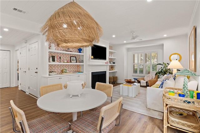 dining space with ceiling fan, a large fireplace, and wood-type flooring