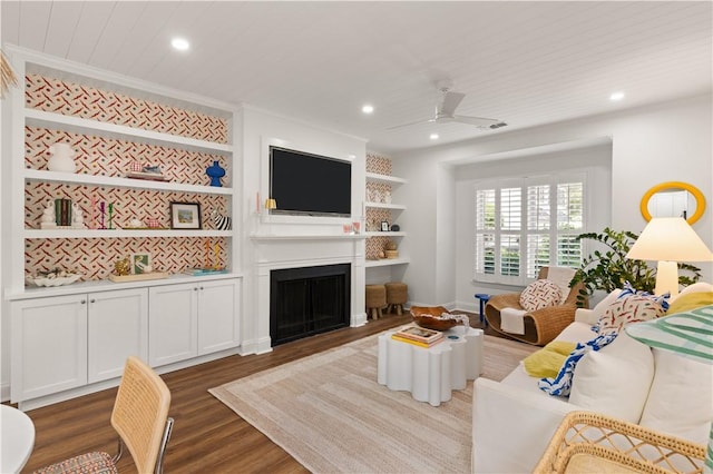 living room featuring built in shelves, ceiling fan, a large fireplace, crown molding, and wood-type flooring