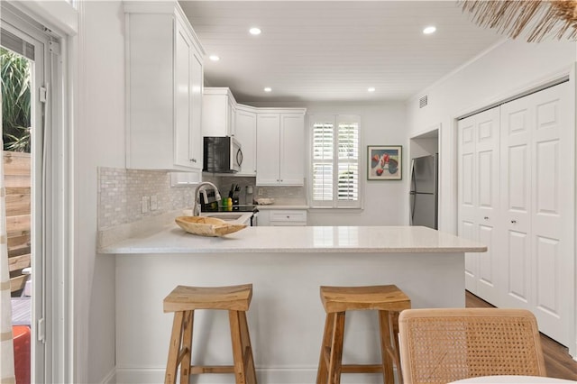 kitchen featuring backsplash, white cabinetry, a kitchen bar, kitchen peninsula, and stainless steel appliances