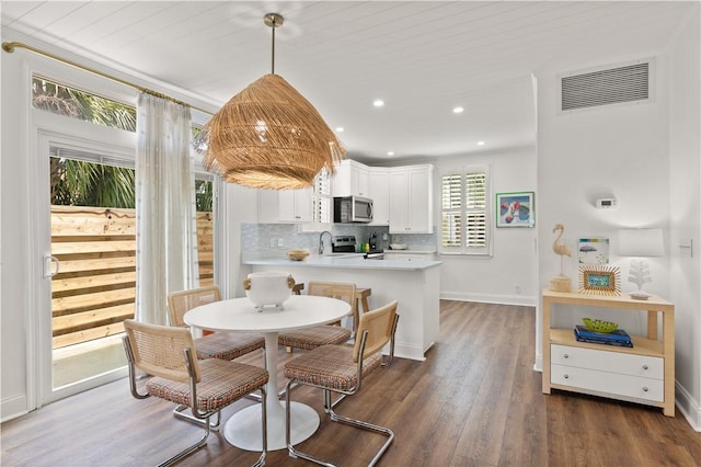 kitchen with kitchen peninsula, dark hardwood / wood-style flooring, stainless steel appliances, pendant lighting, and white cabinets