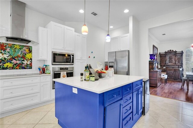 kitchen with wall chimney range hood, light tile patterned floors, blue cabinetry, and stainless steel appliances