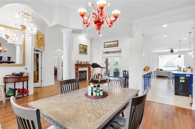 dining room featuring arched walkways, french doors, light wood-type flooring, a glass covered fireplace, and crown molding