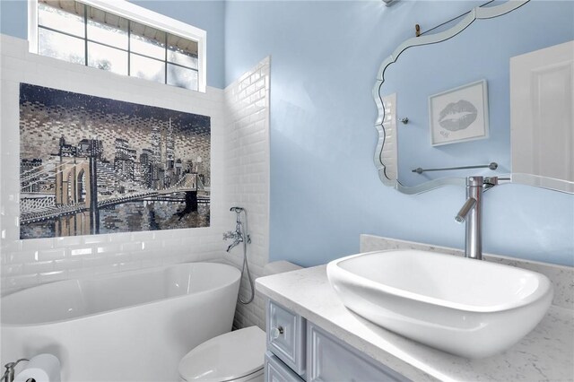 full bathroom with toilet, a soaking tub, and vanity