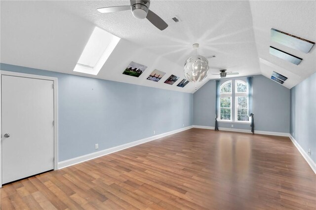 bonus room featuring vaulted ceiling with skylight, baseboards, a ceiling fan, wood finished floors, and a textured ceiling