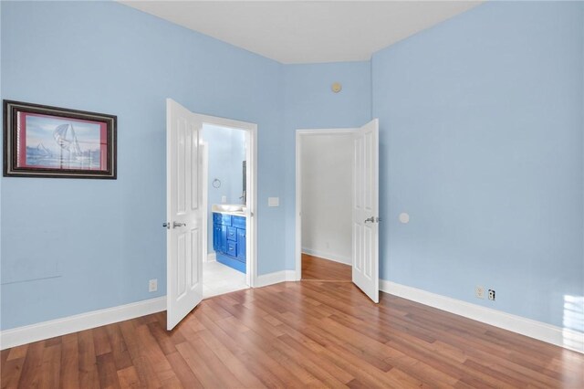 unfurnished bedroom with baseboards, connected bathroom, and light wood-style floors