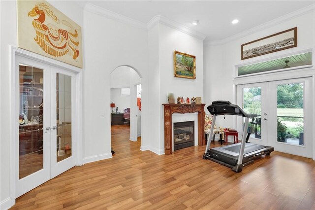 workout area featuring arched walkways, a glass covered fireplace, wood finished floors, crown molding, and french doors