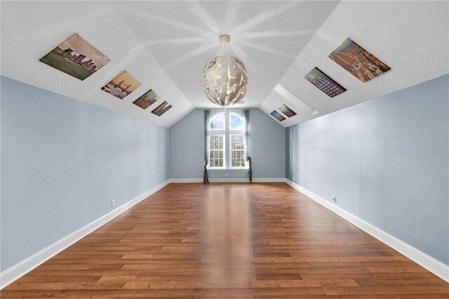 additional living space featuring lofted ceiling, baseboards, a notable chandelier, and wood finished floors