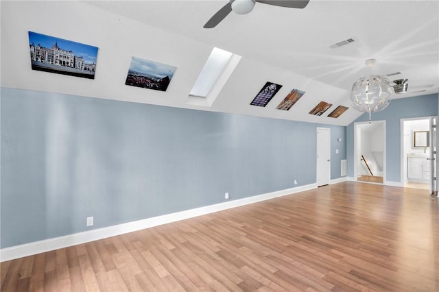 empty room with vaulted ceiling with skylight, visible vents, baseboards, and wood finished floors