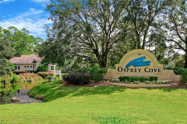 community sign with a water view and a lawn