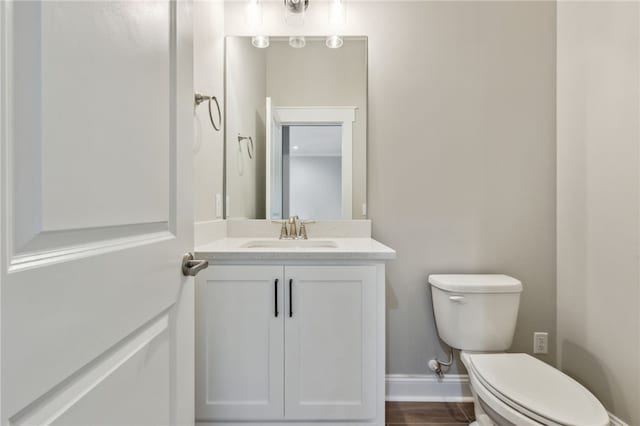 half bathroom featuring vanity, toilet, wood finished floors, and baseboards