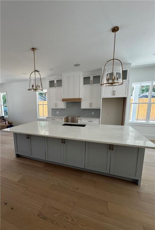 1912 First Ave, Saint Simons Island, GA 31522 - kitchen with white cabinetry, a large island with sink, light countertops, light wood-type flooring, and plenty of natural light