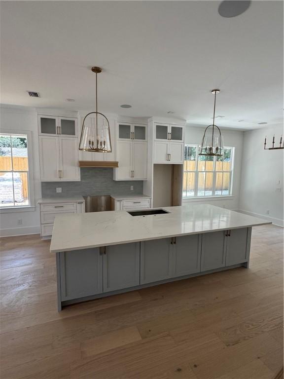 1912 First Ave, Saint Simons Island, GA 31522 - kitchen featuring a chandelier, white cabinets, light wood-type flooring, a spacious island, and glass insert cabinets