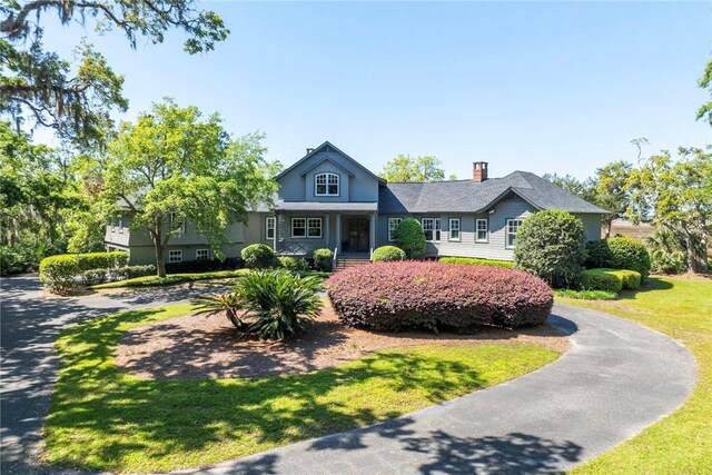 view of front of house featuring a chimney, a front yard, and curved driveway