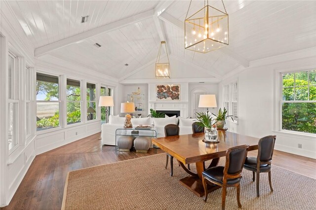 dining area featuring wood finished floors, a chandelier, vaulted ceiling with beams, a fireplace, and visible vents