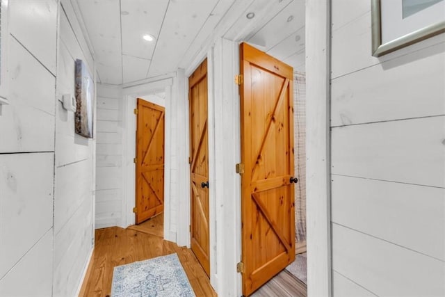 hallway with recessed lighting, light wood-style flooring, and wooden walls
