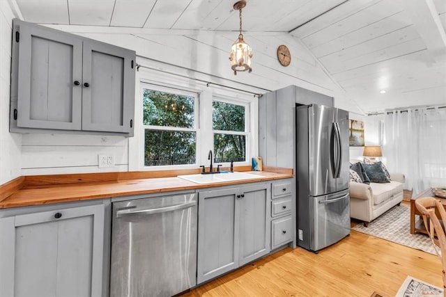 kitchen with appliances with stainless steel finishes, gray cabinets, vaulted ceiling, pendant lighting, and a sink