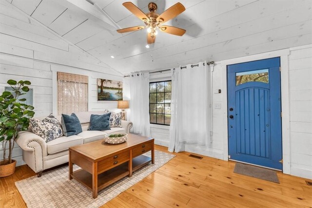 living area with wooden walls, visible vents, a ceiling fan, lofted ceiling, and hardwood / wood-style floors
