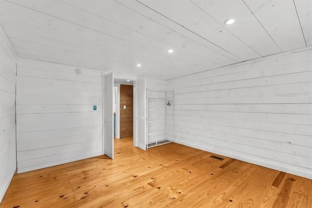 empty room with hardwood / wood-style flooring, recessed lighting, visible vents, and wooden walls