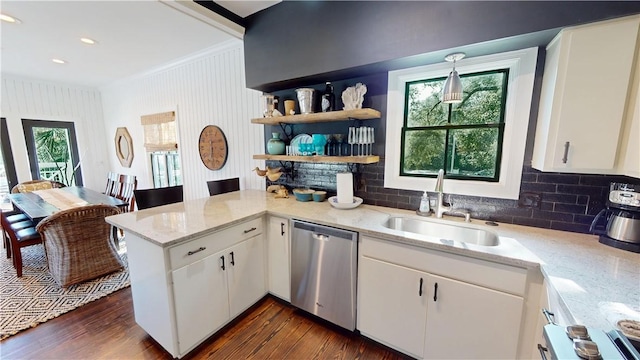 kitchen featuring light stone counters, a peninsula, stainless steel dishwasher, white cabinetry, and a sink