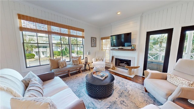 living area featuring a glass covered fireplace, wood finished floors, a wealth of natural light, and crown molding