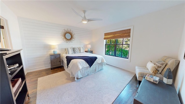 bedroom with wood walls, dark wood finished floors, a ceiling fan, and baseboards