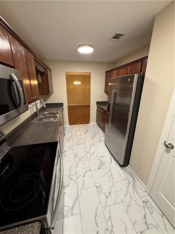 kitchen with sink, stainless steel appliances, dark brown cabinetry, a textured ceiling, and a chandelier