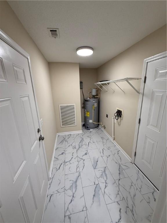 washroom with water heater, hookup for a washing machine, and a textured ceiling