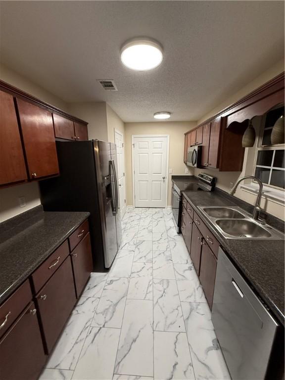 kitchen featuring appliances with stainless steel finishes, sink, a textured ceiling, and dark brown cabinetry