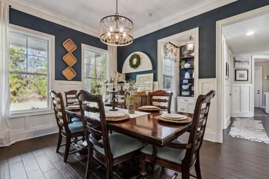 dining room with dark wood-type flooring, ornamental molding, wainscoting, a notable chandelier, and a decorative wall