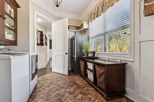 washroom with washing machine and clothes dryer, baseboards, brick floor, and ornamental molding