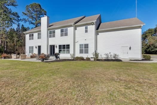 rear view of house featuring a patio, a lawn, an outdoor living space, and a chimney