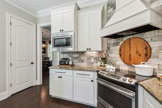 kitchen featuring tasteful backsplash, light stone countertops, premium range hood, appliances with stainless steel finishes, and white cabinetry