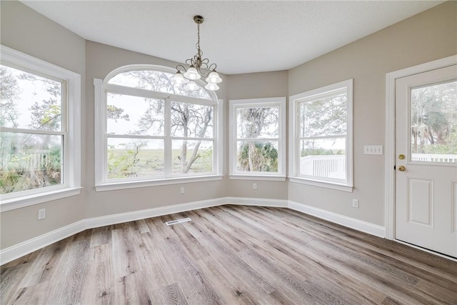 unfurnished dining area with a chandelier, a wealth of natural light, and wood-type flooring