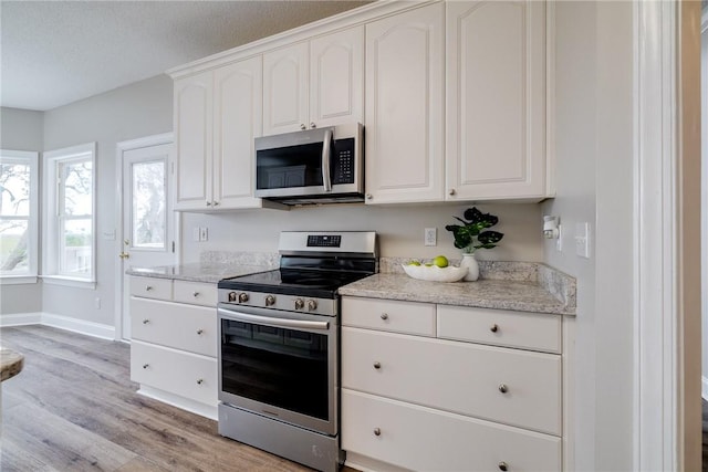 kitchen featuring light stone countertops, stainless steel appliances, light hardwood / wood-style floors, a textured ceiling, and white cabinets