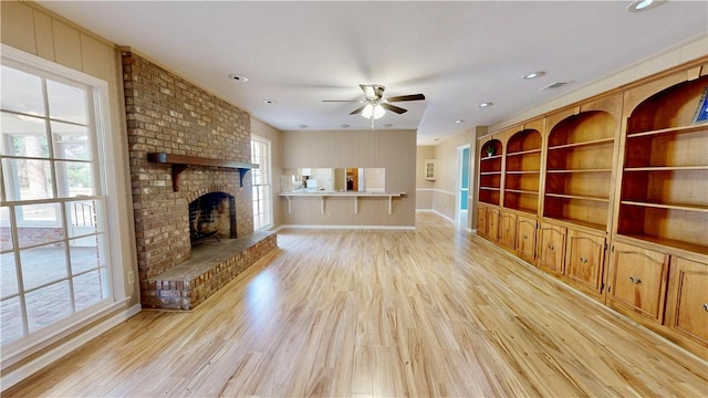 unfurnished living room with a brick fireplace, built in features, light hardwood / wood-style floors, and ceiling fan