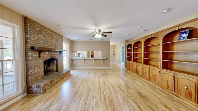 unfurnished living room with ceiling fan, built in features, a brick fireplace, and light hardwood / wood-style flooring