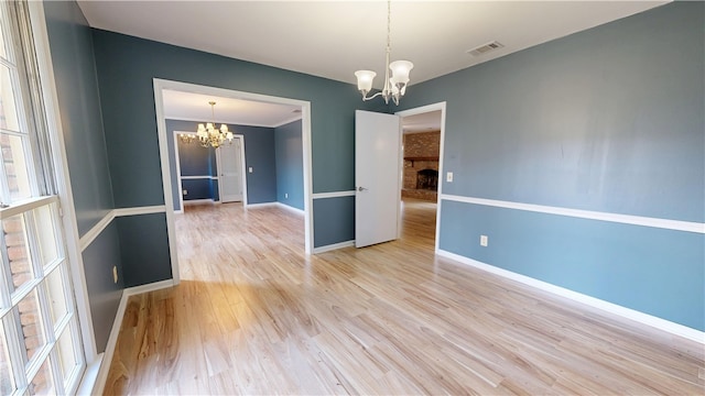 spare room featuring a fireplace, a chandelier, and light hardwood / wood-style flooring