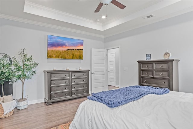 bedroom featuring ceiling fan, light wood-type flooring, crown molding, and a tray ceiling