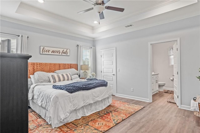 bedroom featuring a raised ceiling, ensuite bath, hardwood / wood-style flooring, ceiling fan, and ornamental molding