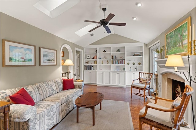 living area with vaulted ceiling with skylight, built in shelves, visible vents, a ceiling fan, and a lit fireplace