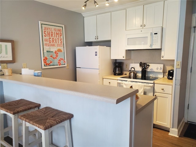 kitchen with white appliances, white cabinetry, a breakfast bar, and dark wood-type flooring